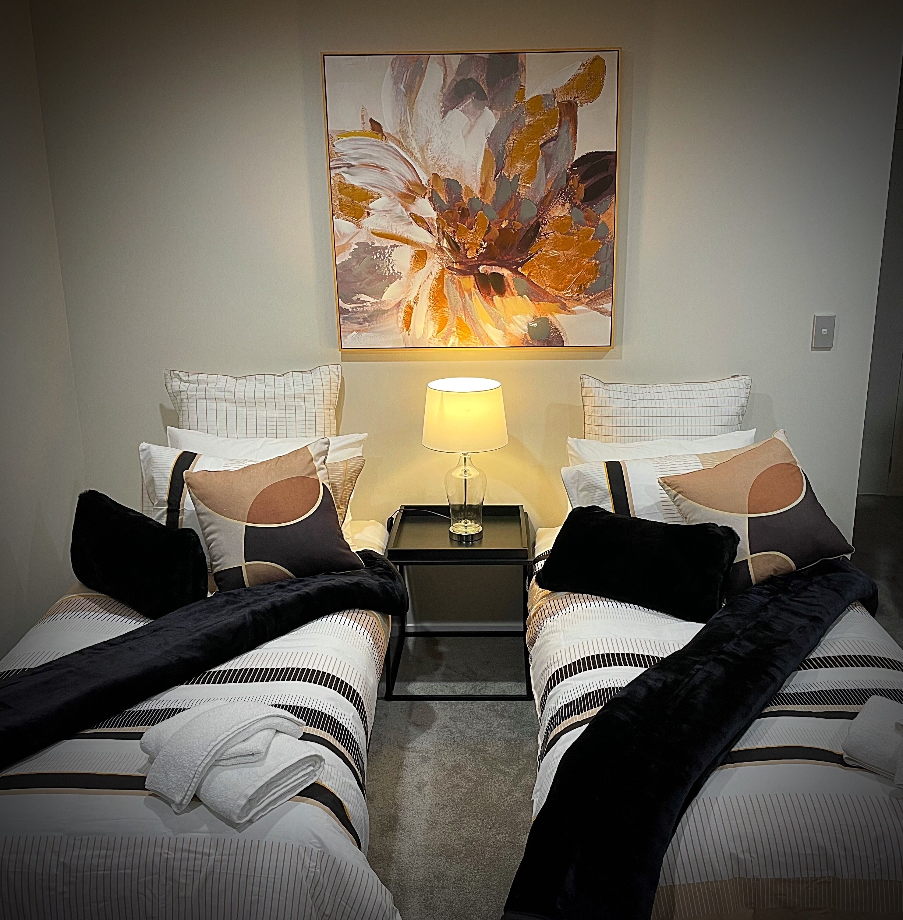 A hotel room with two beds, a nightstand with a lamp, and a large abstract painting on the wall.