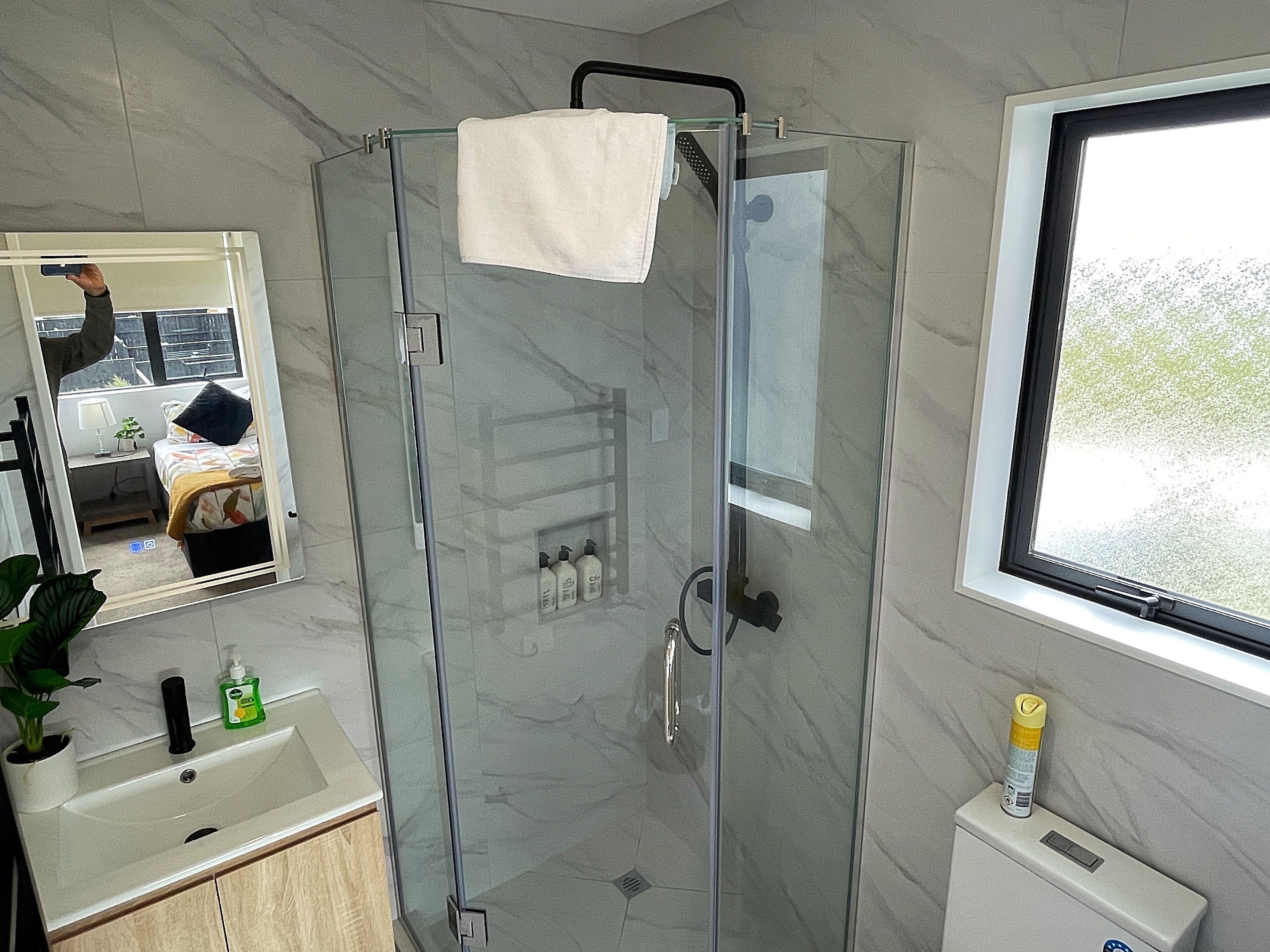 A modern bathroom with a glass shower enclosure, a sink with a mirror, and a window with a view of greenery.