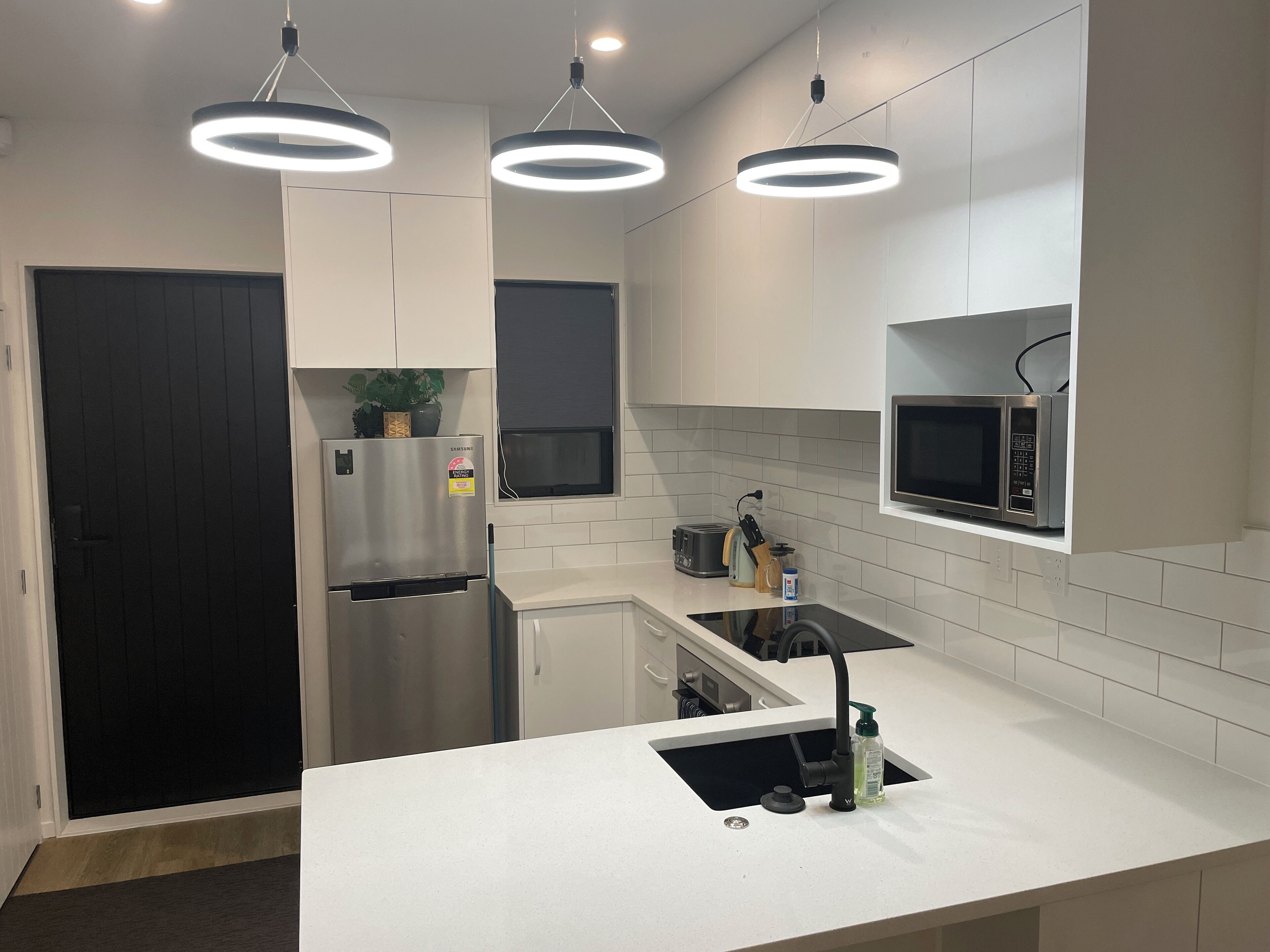 Een moderne keuken met witte kasten, een roestvrijstalen koelkast, een magnetron en een gootsteen met een kraan.