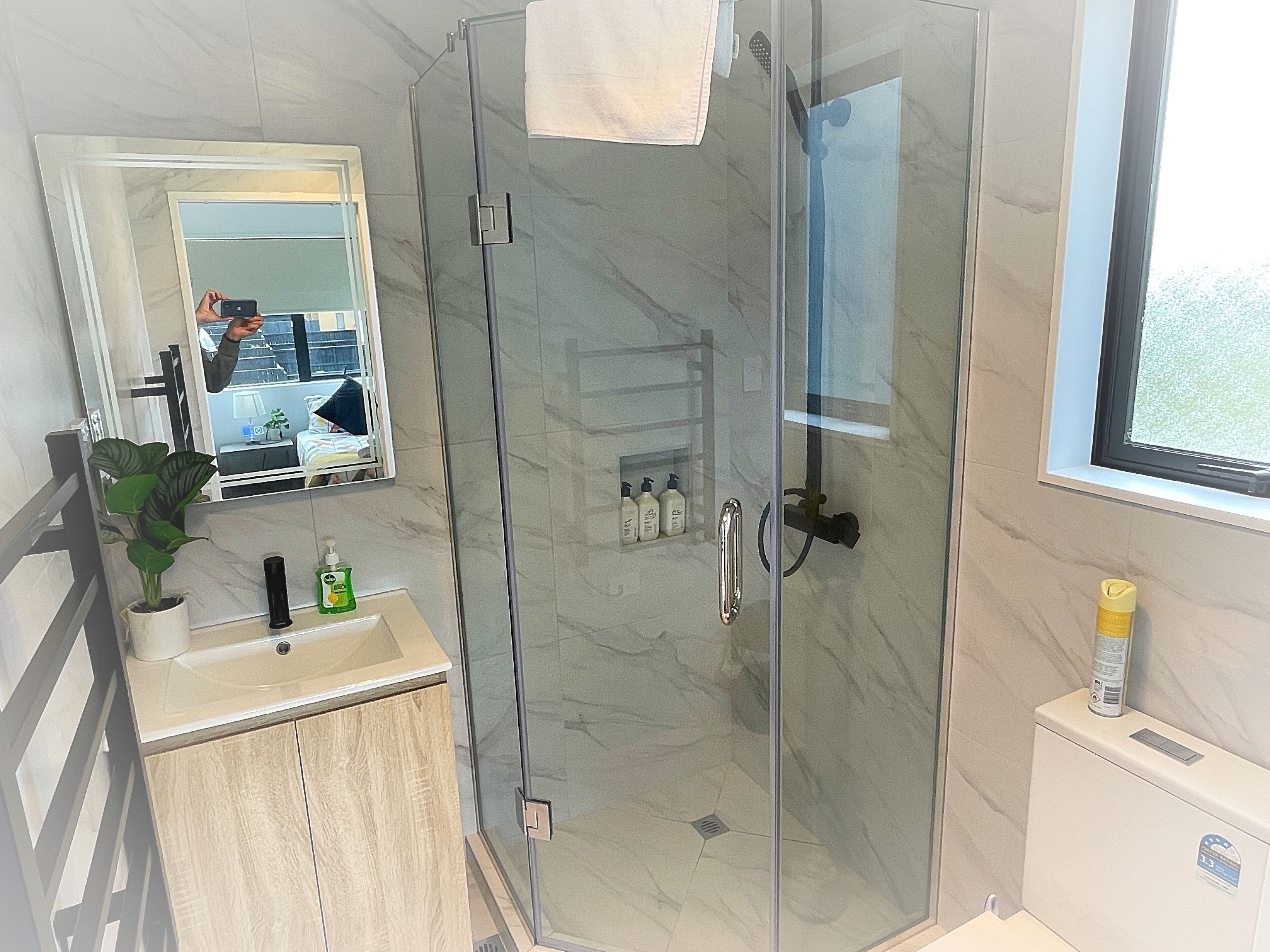 Un baño moderno con ducha de vidrio, lavamanos con artículos de aseo y un espejo que refleja la habitación.