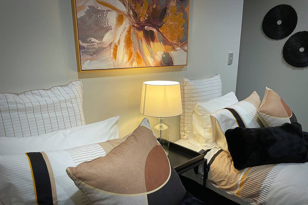 Ett hotellrum med två sängar, ett nattduksbord med en lampa, ett konstverk som hänger på väggen och två vinylskivor.