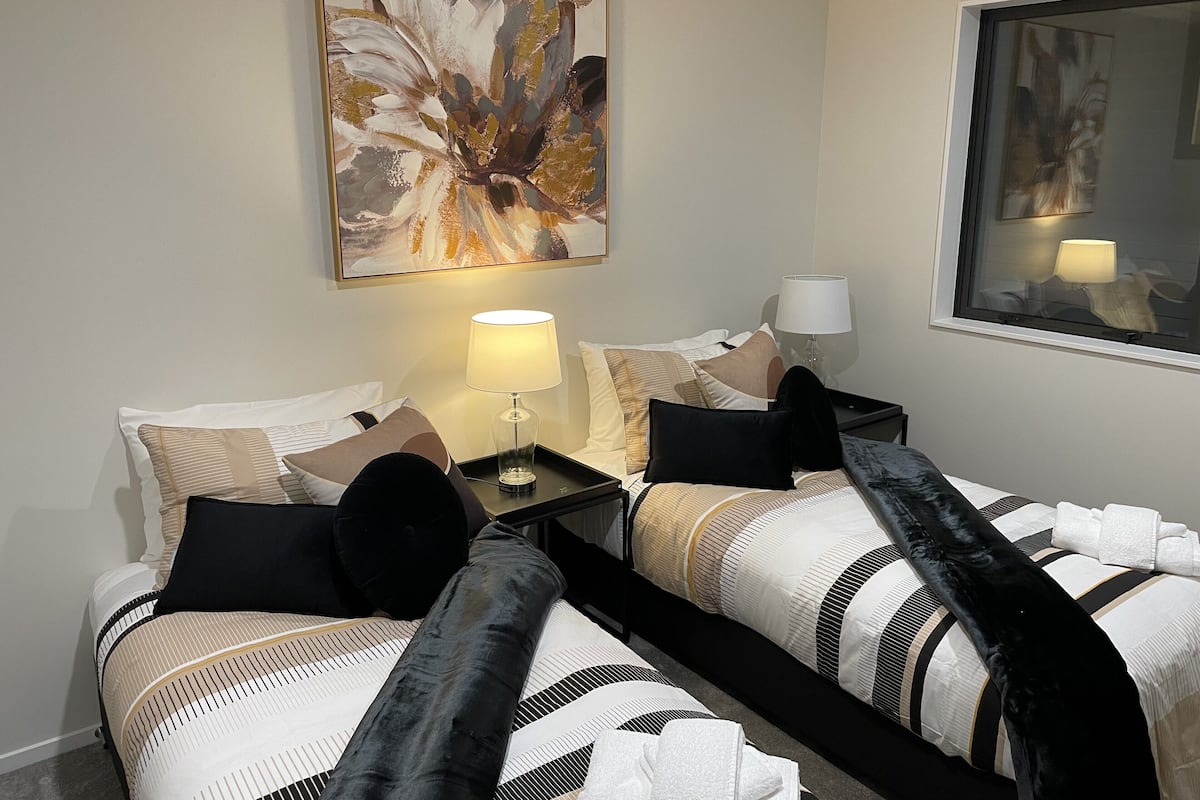 Ett hotellrum med två sängar, en stor, abstrakt målning på väggen, ett fönster med utsikt och ett nattduksbord med en lampa.