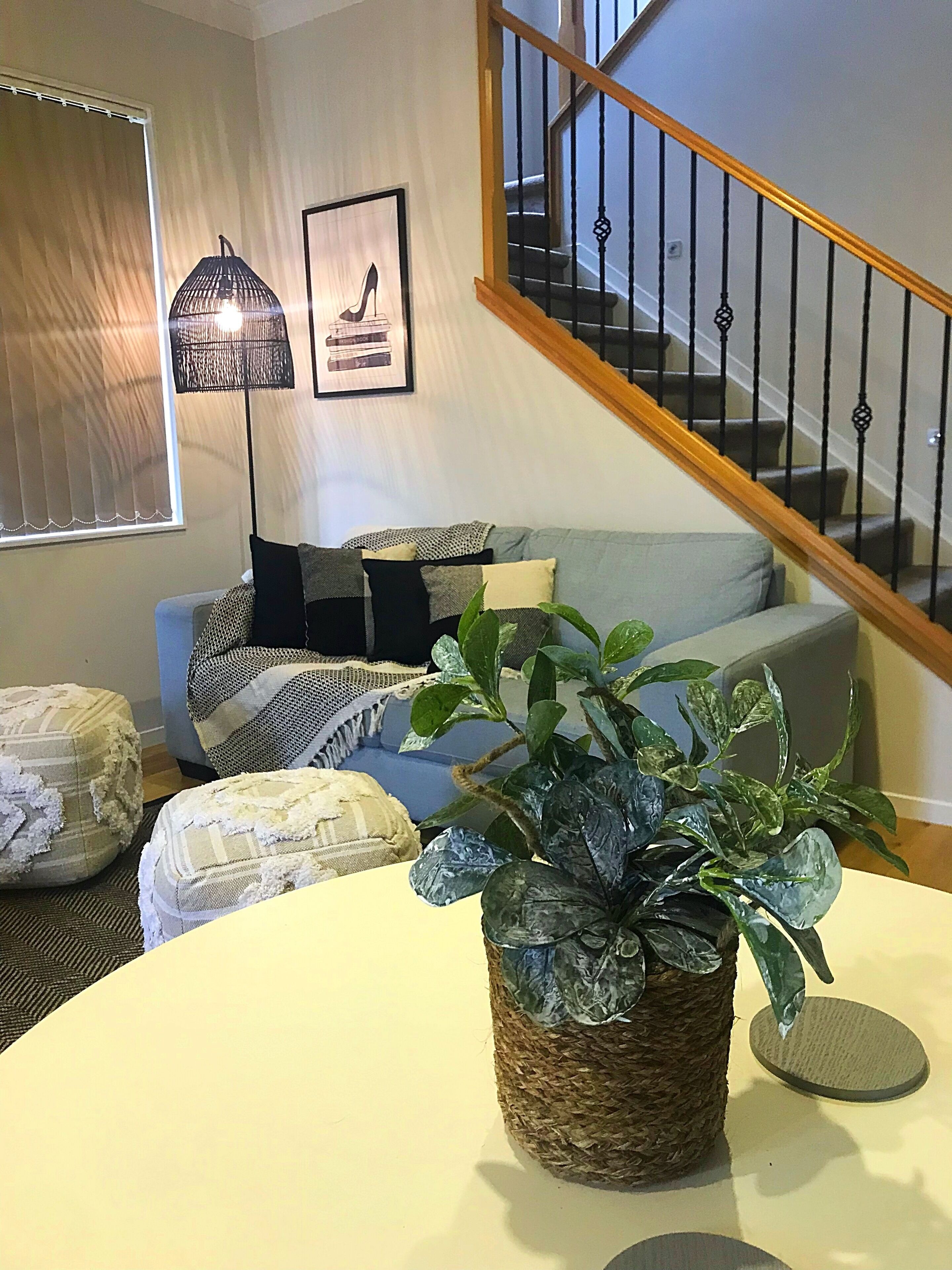 En stue med sofa, puder, sofabord, en stueplante, gulvlampe og trappe.