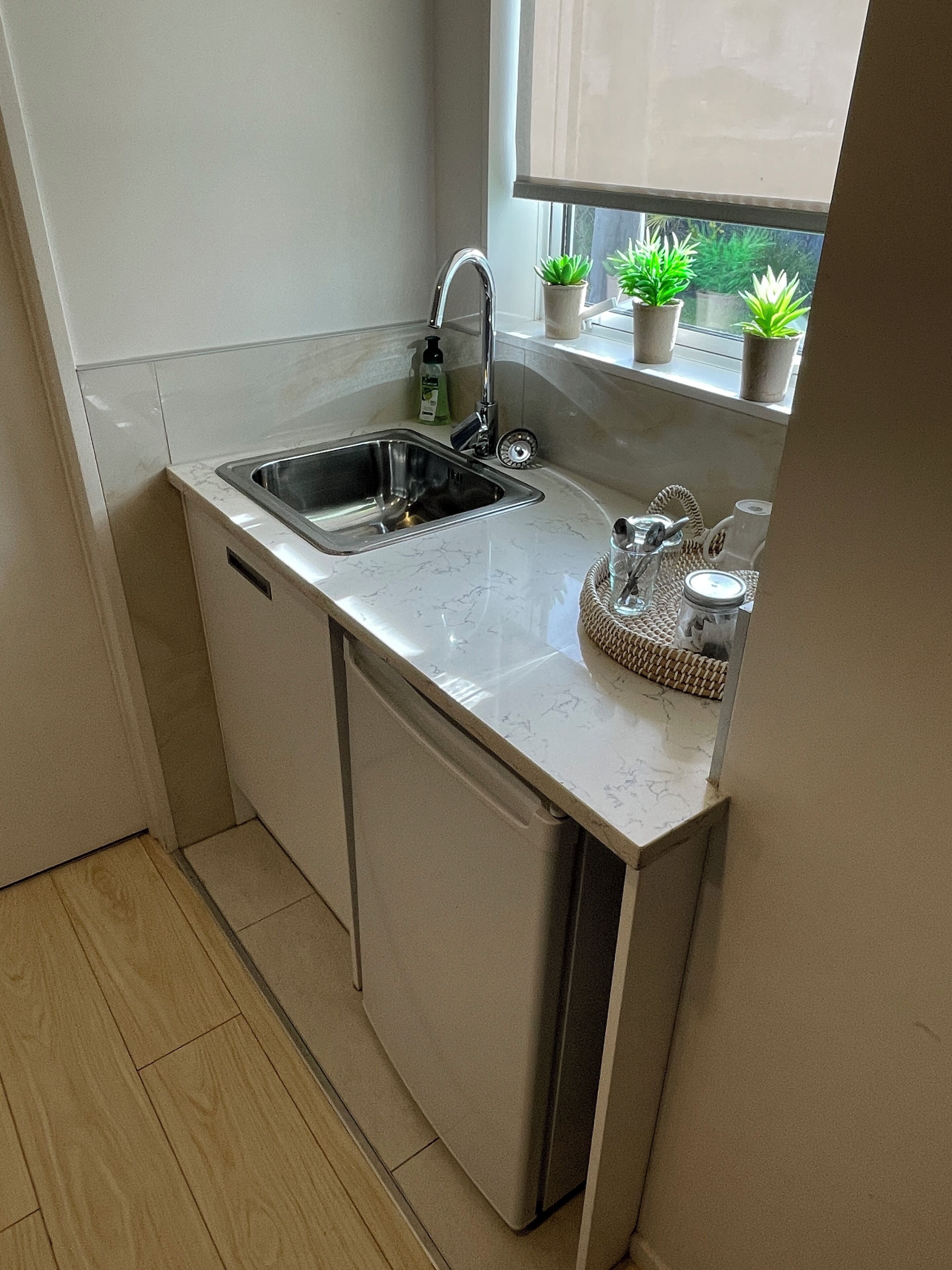 A compact kitchen with a sink, a window with potted plants, and a built-in dishwasher.