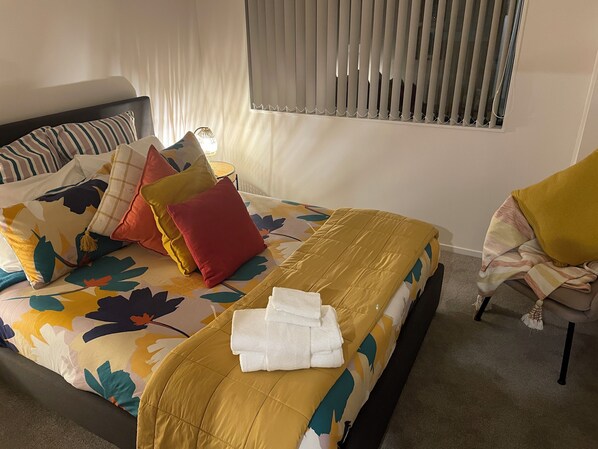 A neatly made bed with a floral bedspread, pillows, and a folded towel. - Flatbush Holiday Accommodation (Auckland)