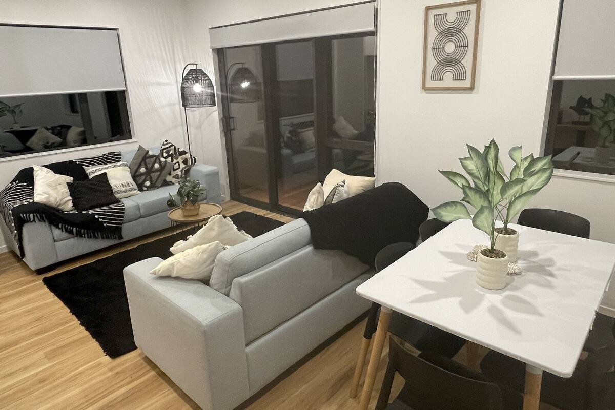 Ett modernt vardagsrum med en grå soffa, ett litet bord med en växt och en matplats med ett vitt bord.