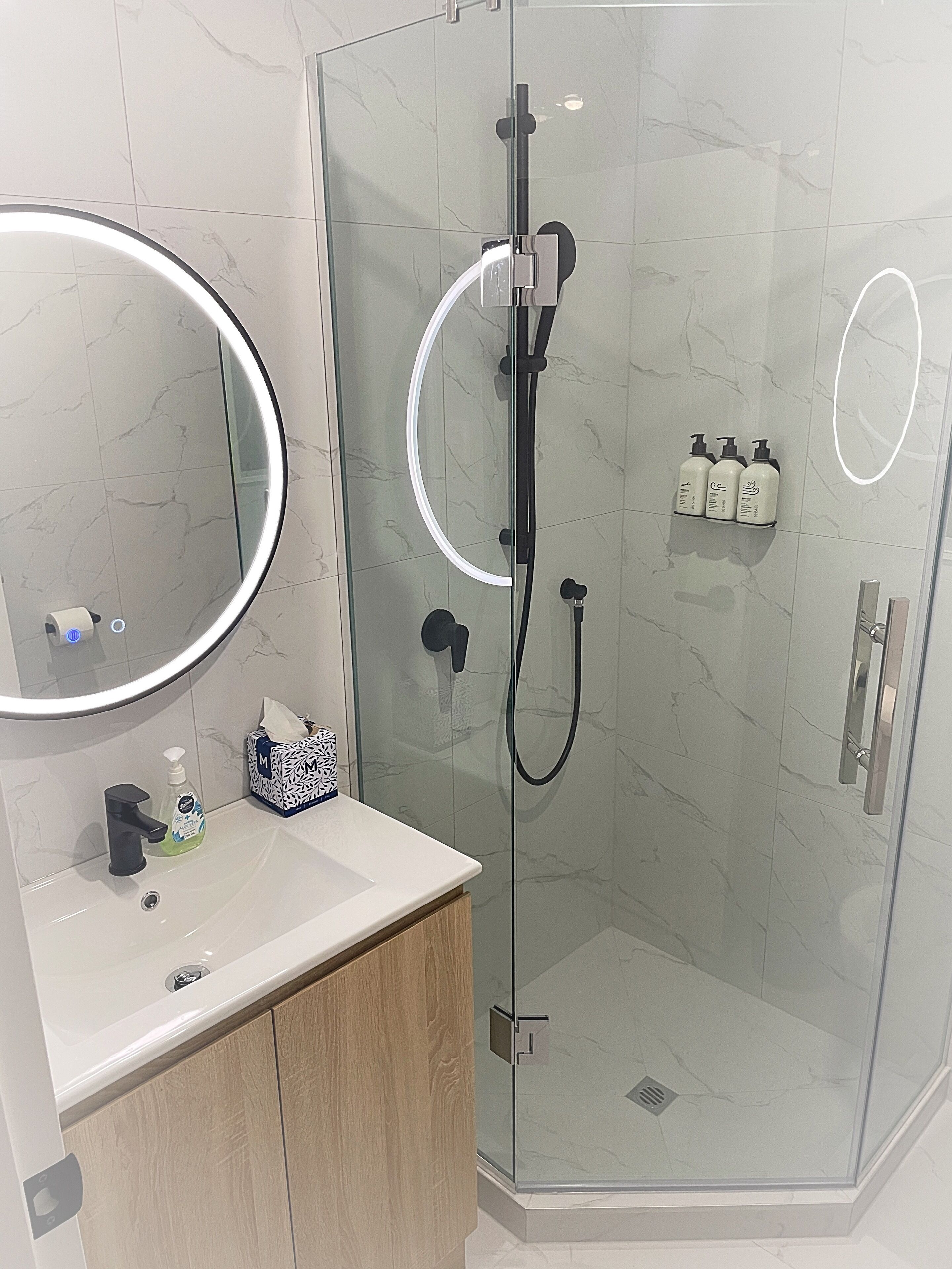 Un baño moderno con ducha de vidrio, tocador con espejo y artículos de aseo en la pared.