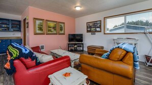 Ein Wohnzimmer mit einem roten Sofa, einem braunen Ledercouch, einem Fernseher, gerahmten Bildern an der Wand und einem Fenster mit Jalousien.