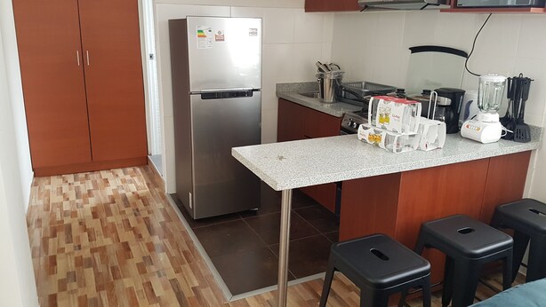Eine kompakte Küche mit Kühlschrank, Mikrowelle, Kaffeemaschine und Mixer. Es gibt Hocker und eine kleine Bar.