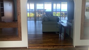An interior space with a wooden floor, a sofa, and a dining area with a view of the ocean.