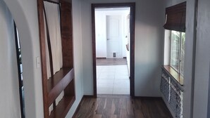 A spacious room with a wooden floor, a large window with a view, and a door leading to another room.