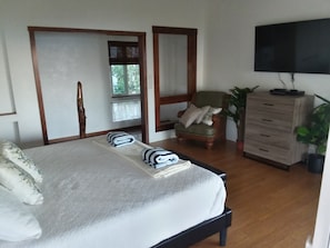A bedroom with a bed, a wooden chair, a television, a dresser, and a window with curtains.