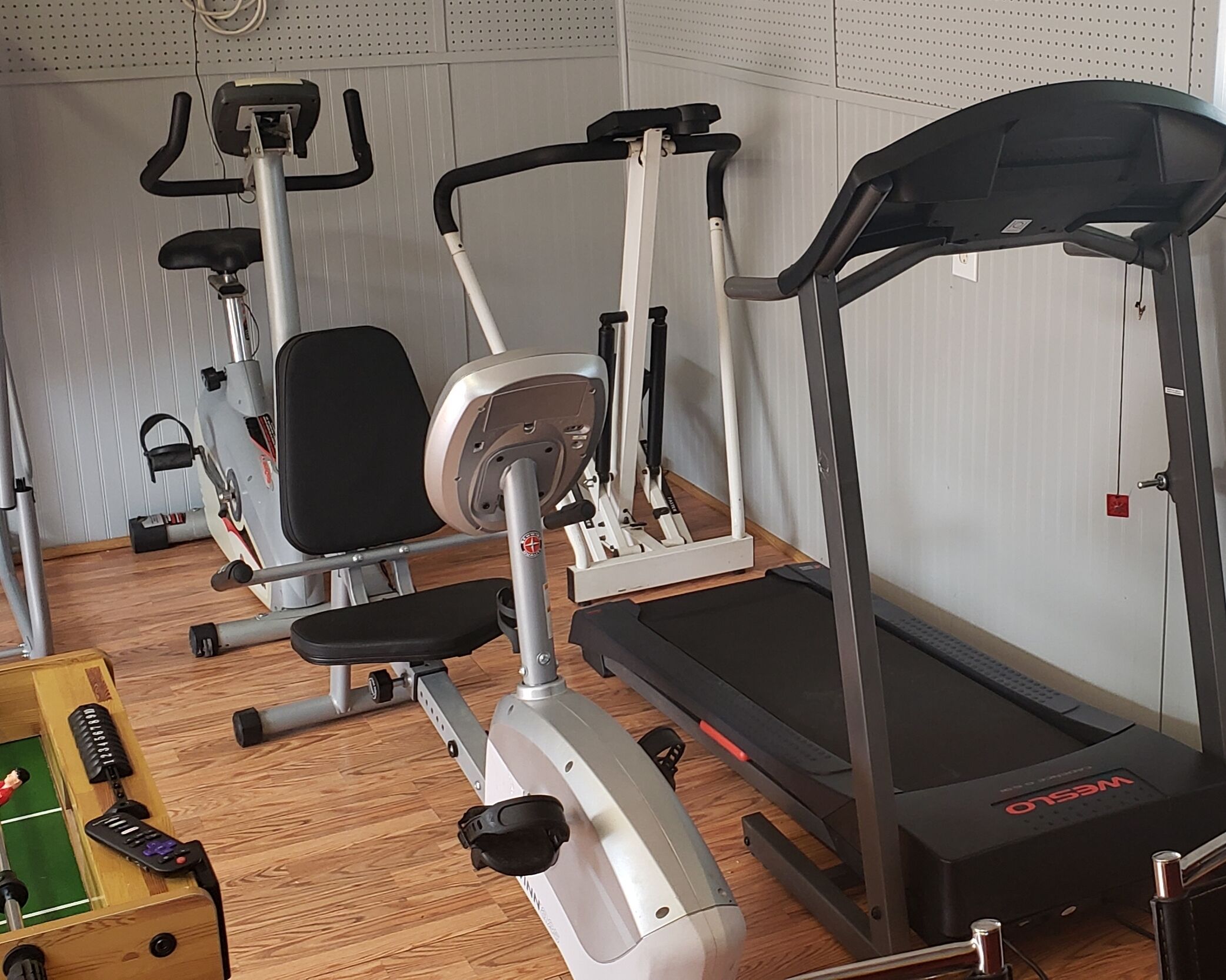 Un gimnasio con cinta de correr, elíptica y banco para pesas.