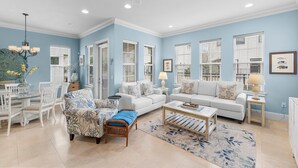A living room with a dining area, featuring a white sofa, a patterned armchair, and a coffee table. - Waterfront ~ Golf Cart ~ Community Pool ~ Patio (Miramar Beach)