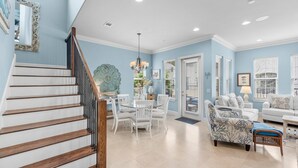 A spacious living room with a staircase, white furniture, and a large window. - Waterfront ~ Golf Cart ~ Community Pool ~ Patio (Miramar Beach)