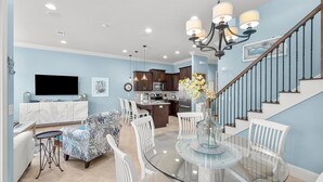 A modern kitchen with dark cabinets, a central island, and a dining area with a glass table and white chairs. - Waterfront ~ Golf Cart ~ Community Pool ~ Patio (Miramar Beach)