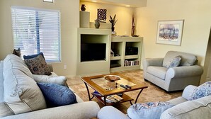 A living room with two sofas, a coffee table, a TV, and shelves with books and decorative items. - STEPS From the Pool! Relax in your Comfy Pool-side Condo! (Oro Valley)