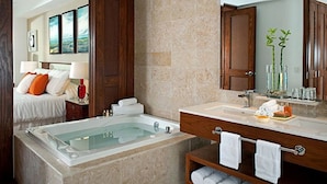 A modern bathroom with a large bathtub, a vanity with a mirror, and a bed in the adjacent room.