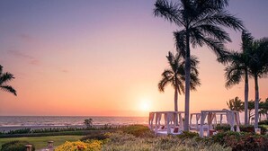A beachside resort with a gazebo and palm trees, overlooking the ocean at sunset.