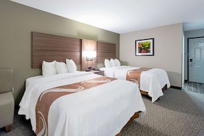 Habitación de hotel con dos camas, cabecera, mesita de noche, una silla y una puerta.