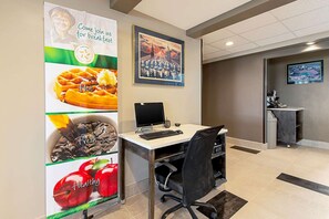 A hotel reception area with a desk, computer, and a banner advertising breakfast options. - Quality Inn of Mishawaka (Mishawaka)