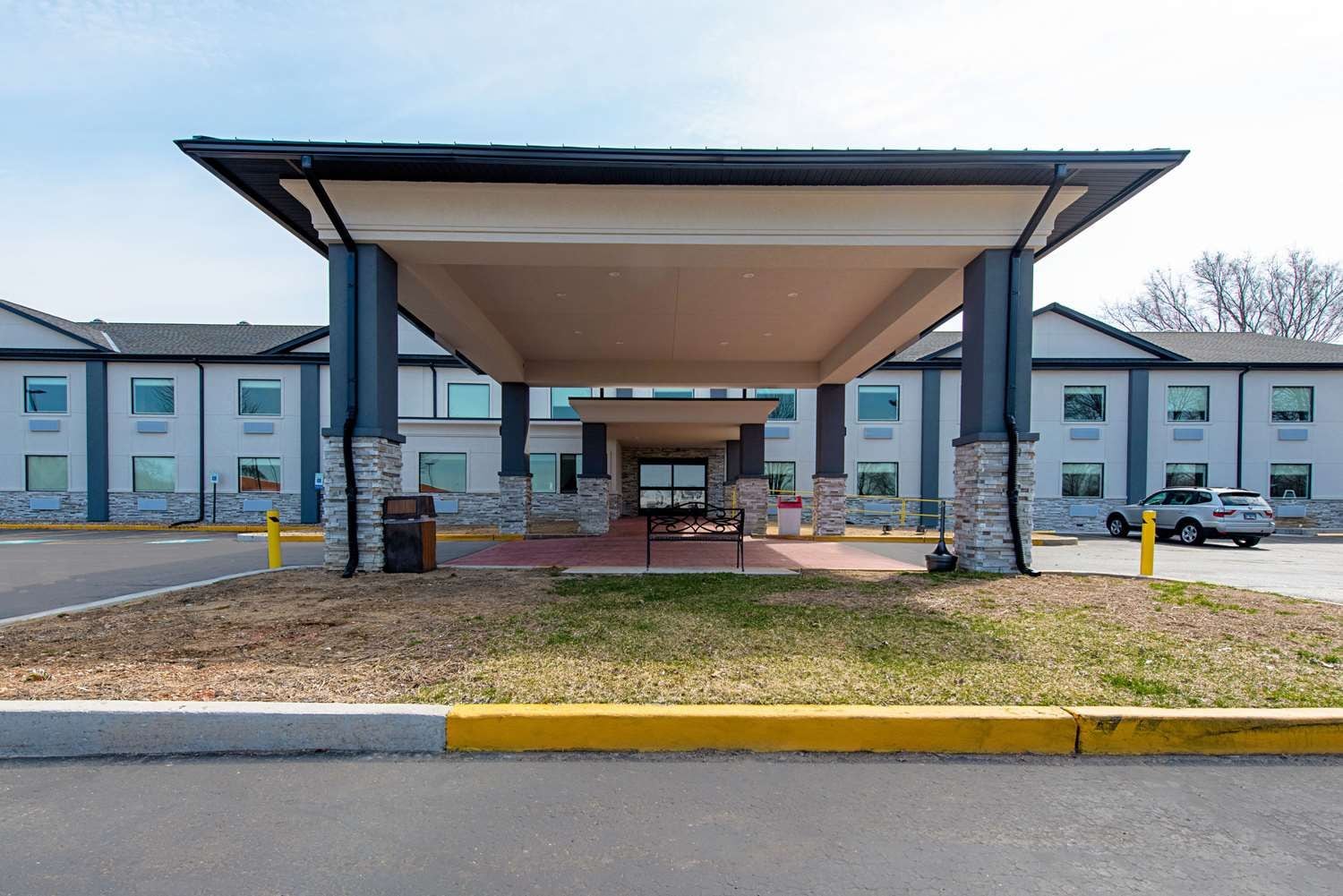 A covered outdoor area with a bench, a trash can, and a car parked nearby.