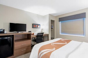 Habitación de hotel con una cama, un escritorio con computadora, televisor y refrigerador pequeño.