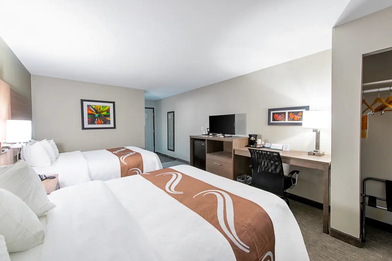 A hotel room with two beds, a desk, a chair, a television, and artwork on the walls.