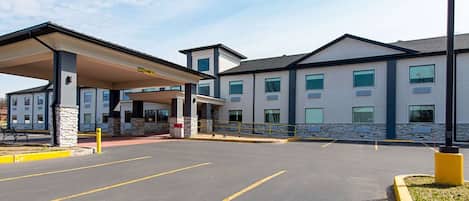 A hotel with a covered entrance, a parking lot, and a building with multiple windows.