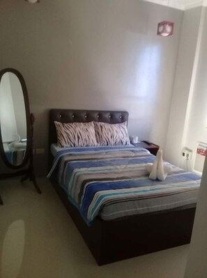 A bedroom with a bed, a nightstand, a mirror, and a wall-mounted light.