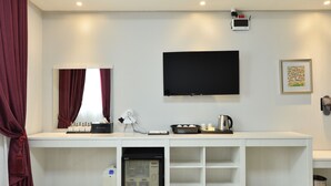 Une chambre d’hôtel moderne avec une console blanche, un téléviseur à écran plat, un petit réfrigérateur, une bouilloire et un tableau encadré au mur.