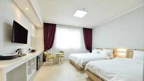 Une chambre d’hôtel avec deux lits, un bureau avec un téléviseur à écran plat, une petite table avec des chaises et une fenêtre avec des rideaux.