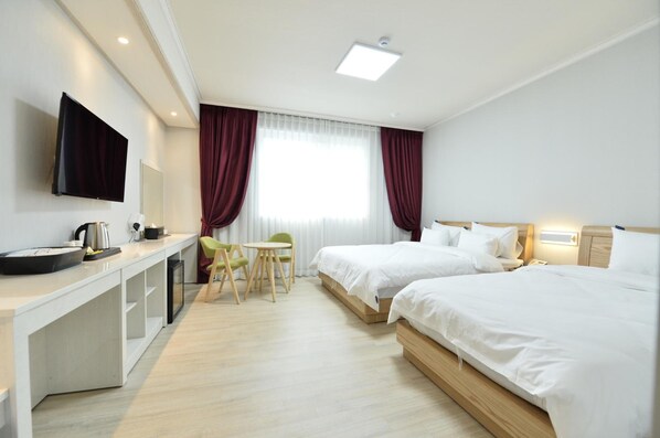 A hotel room with two beds, a desk with a flat-screen TV, a small table with chairs, and a window with curtains. - Gwangju Tourist Hotel (Gwangju)