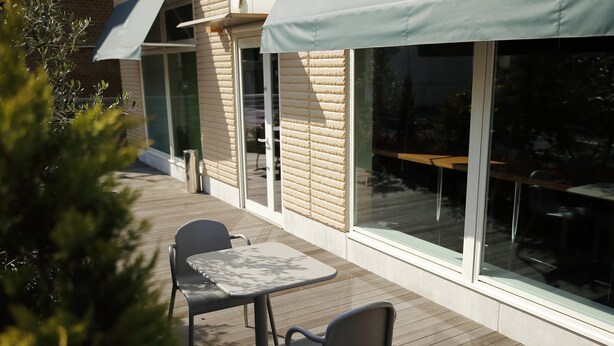 Un patio al aire libre con una mesa, sillas, un muro de ladrillo y ventanas amplias.