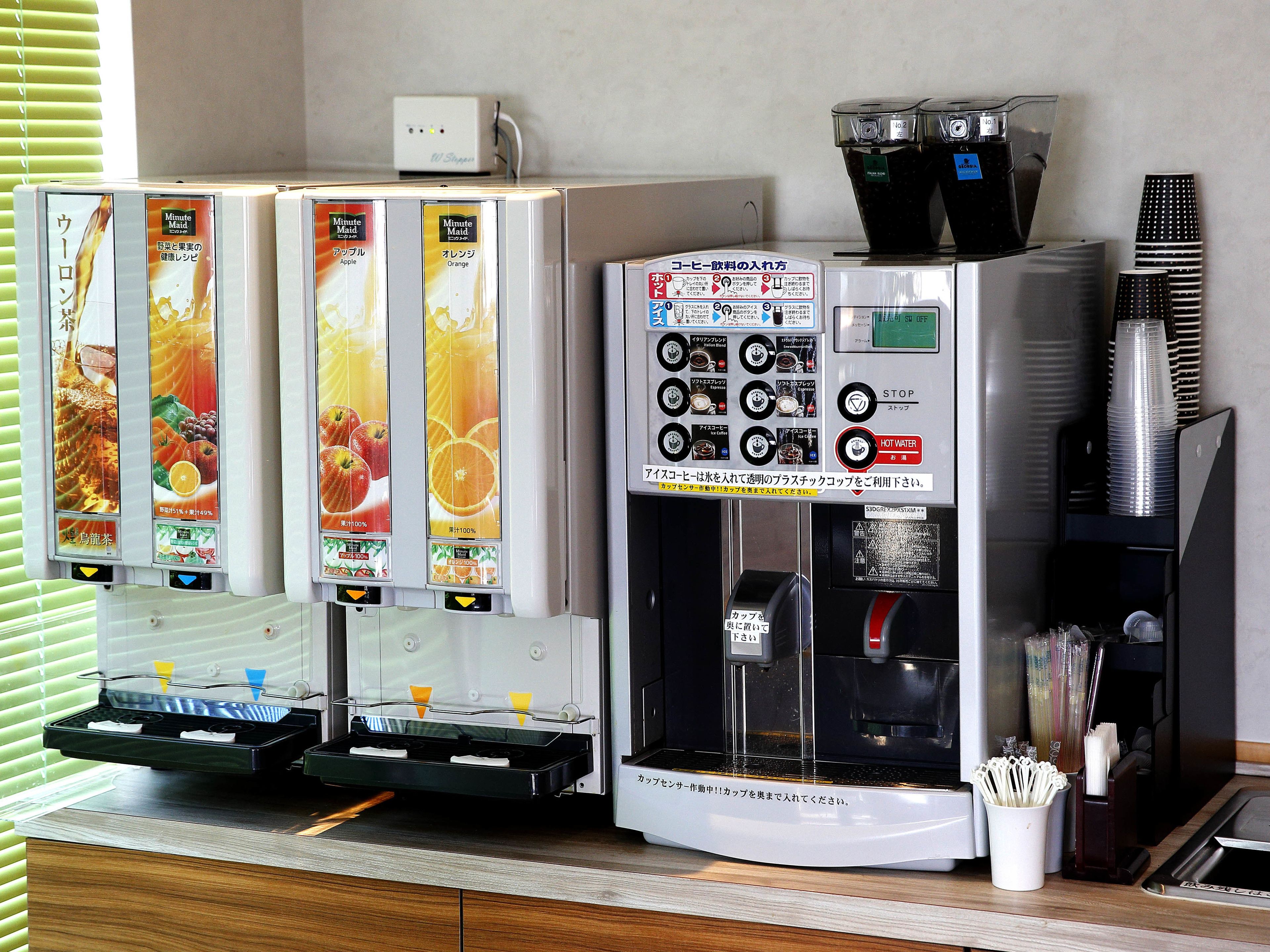 Ein Selbstbedienungsbereich für Getränke mit verschiedenen Auswahlmöglichkeiten, einer Kaffeemaschine und einem Stapel Einwegbechern.