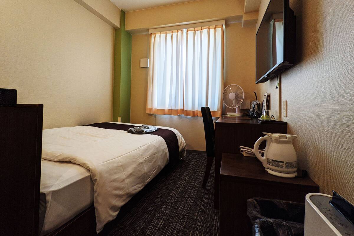 Une chambre d’hôtel avec deux lits, un bureau avec une bouilloire, une chaise, une télévision et une fenêtre avec des rideaux.