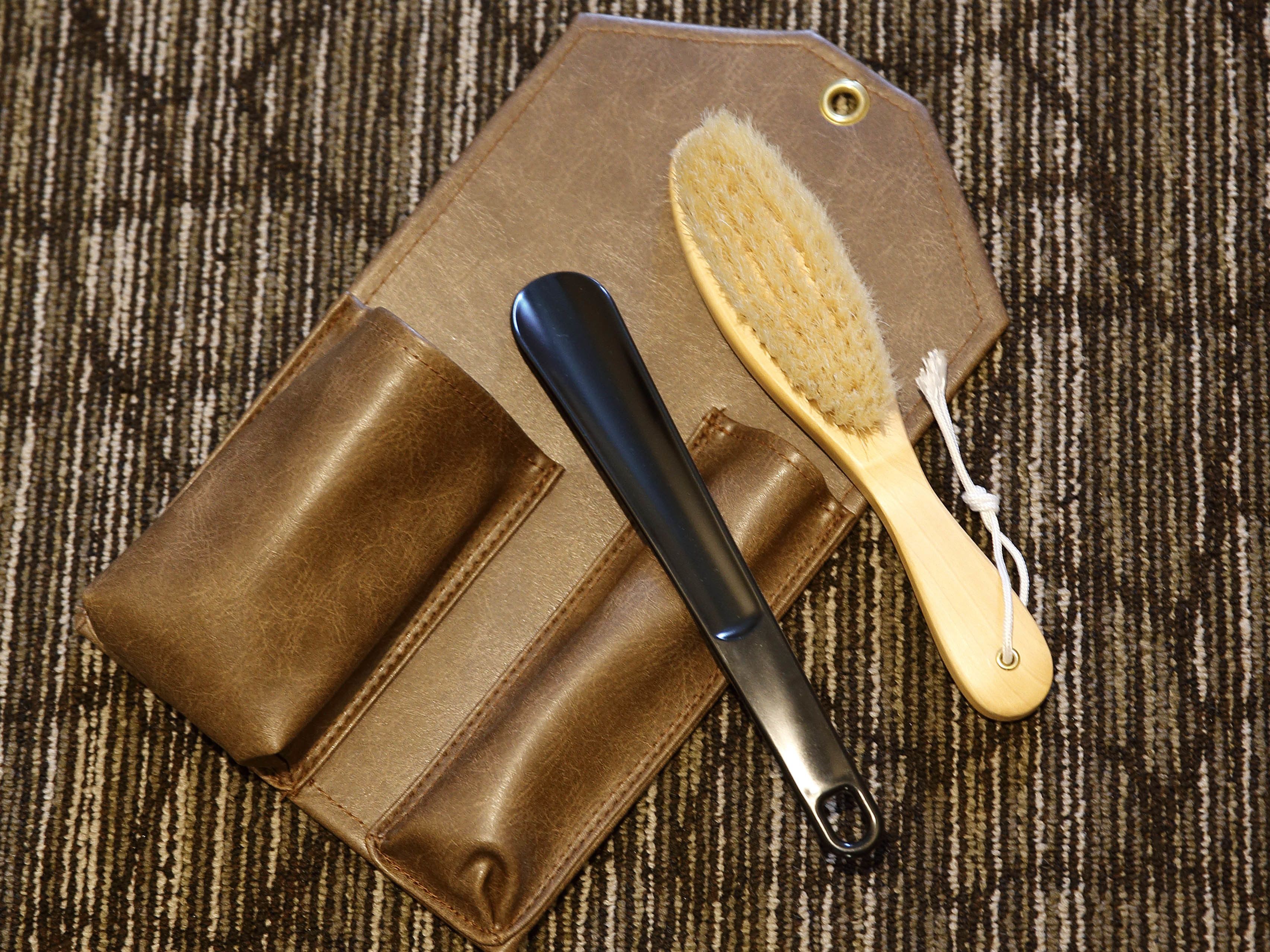 A brown leather case with a metal tool and a wooden brush.