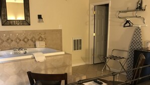 A hotel room with a bathroom, a seating area with a table, and a bed with a patterned bedspread. - The Mountaineer Hotel (Williamson)