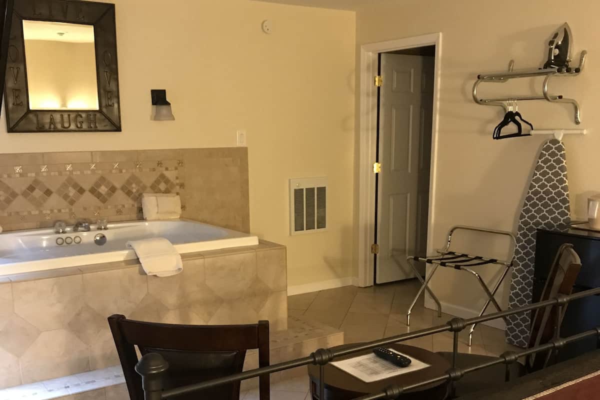 A hotel room with a bathroom, a seating area with a table, and a bed with a patterned bedspread.