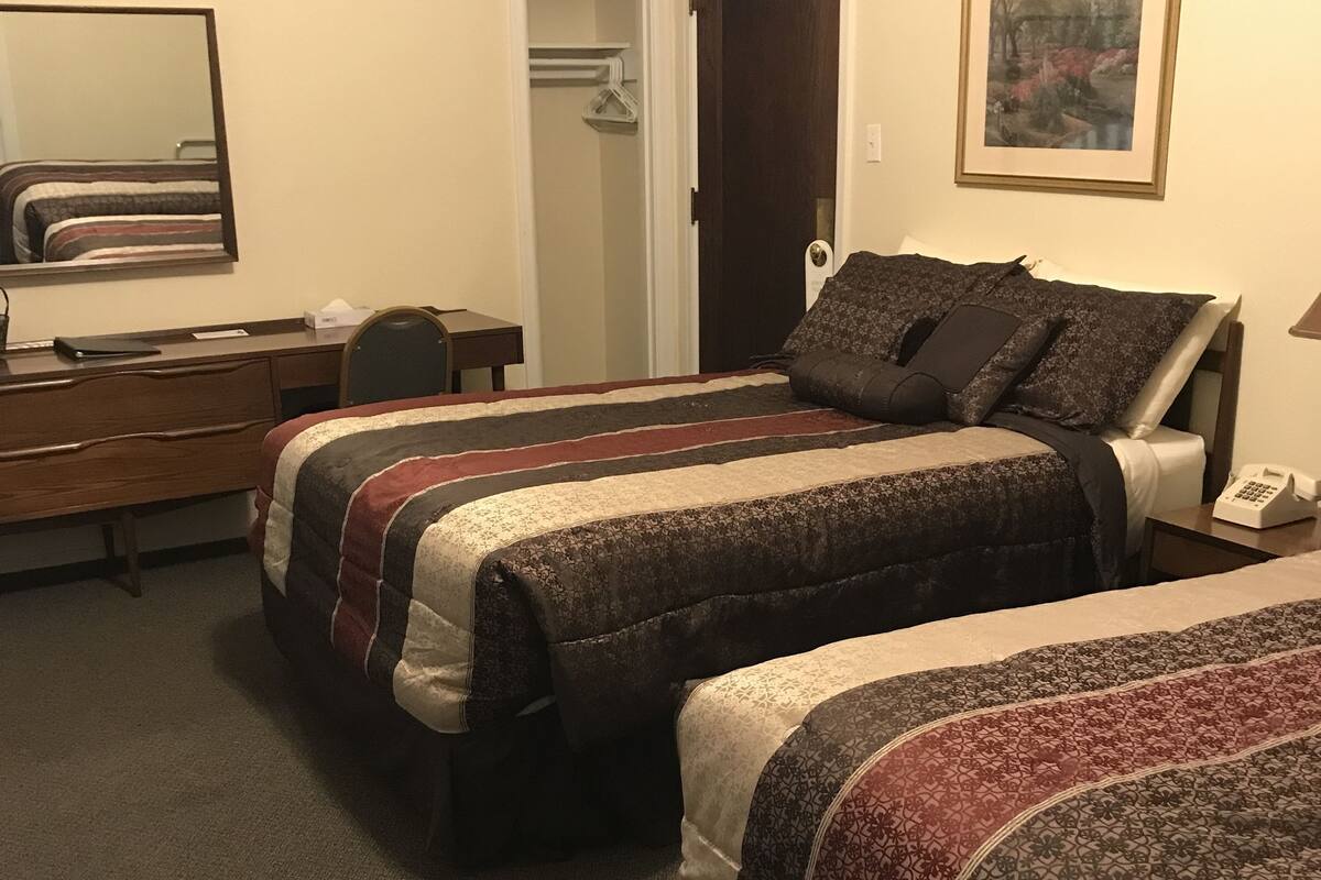 A hotel room with two beds, a desk, a chair, a wardrobe, and a painting on the wall.