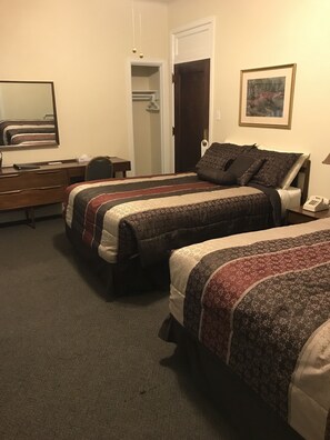 A hotel room with two beds, a desk, a chair, a wardrobe, and a painting on the wall. - The Mountaineer Hotel (Williamson)