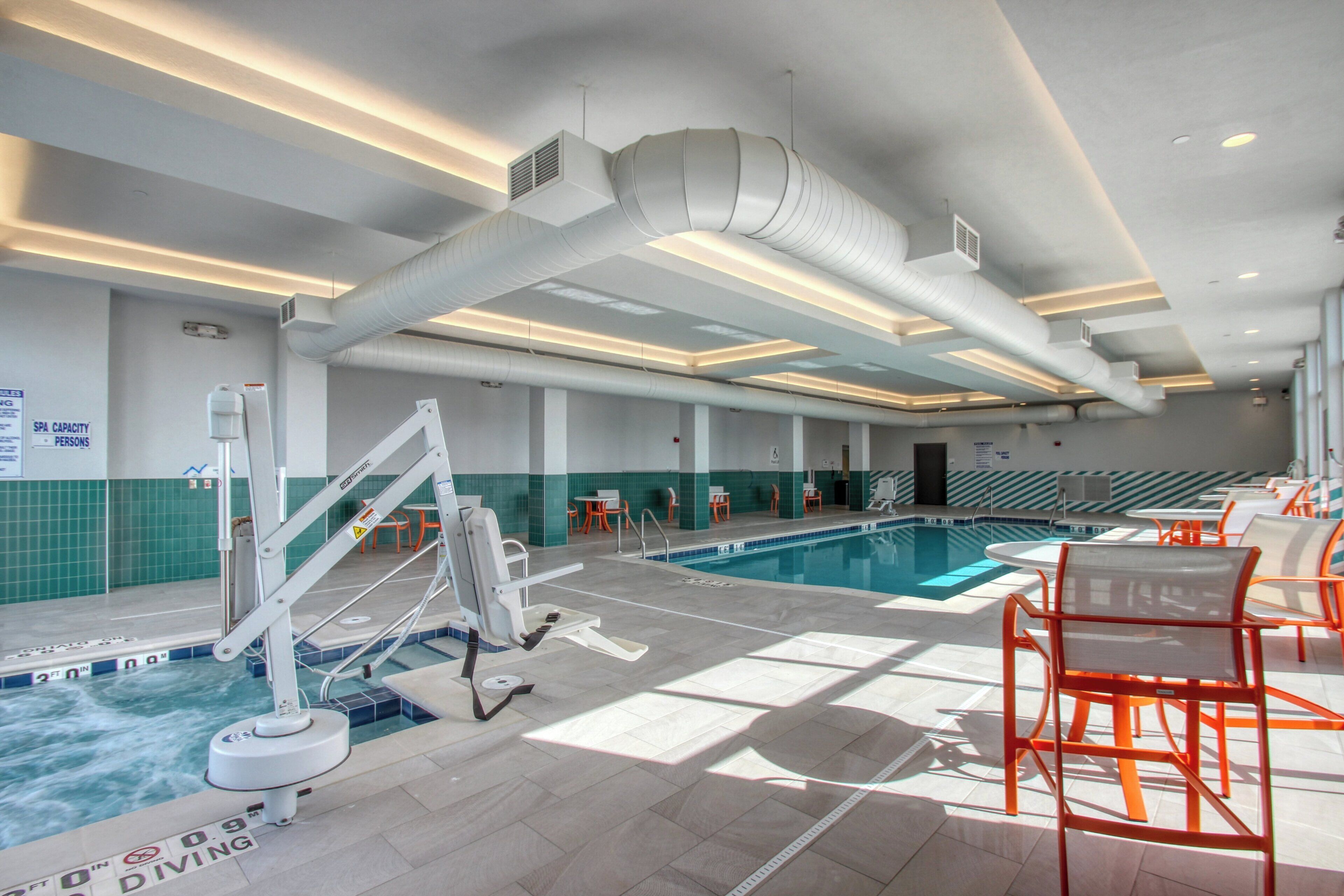 Ein Schwimmbecken mit Sprungbrett, Liegestühlen und einer Decke mit Luftschlitzen.