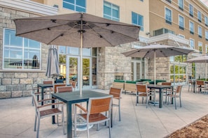 An outdoor patio area with tables and chairs, umbrellas, and a stone building in the background.