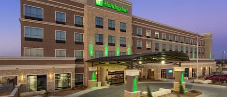 A Holiday Inn hotel with a brick facade, a covered entrance, and a landscaped area with small trees.
