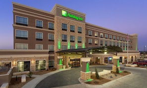A Holiday Inn hotel with a brick facade, a covered entrance, and a landscaped area with small trees.