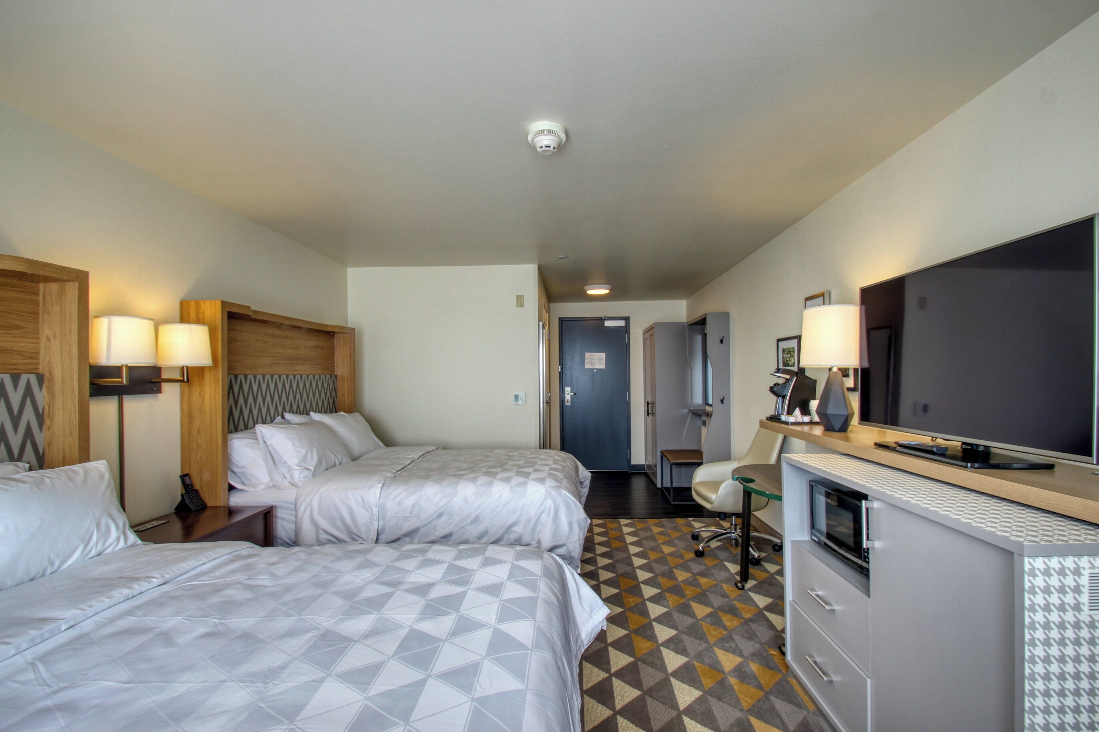 Quarto de hotel com duas camas, uma escrivaninha com televisão de tela plana, micro-ondas e uma pequena cozinha equipada.