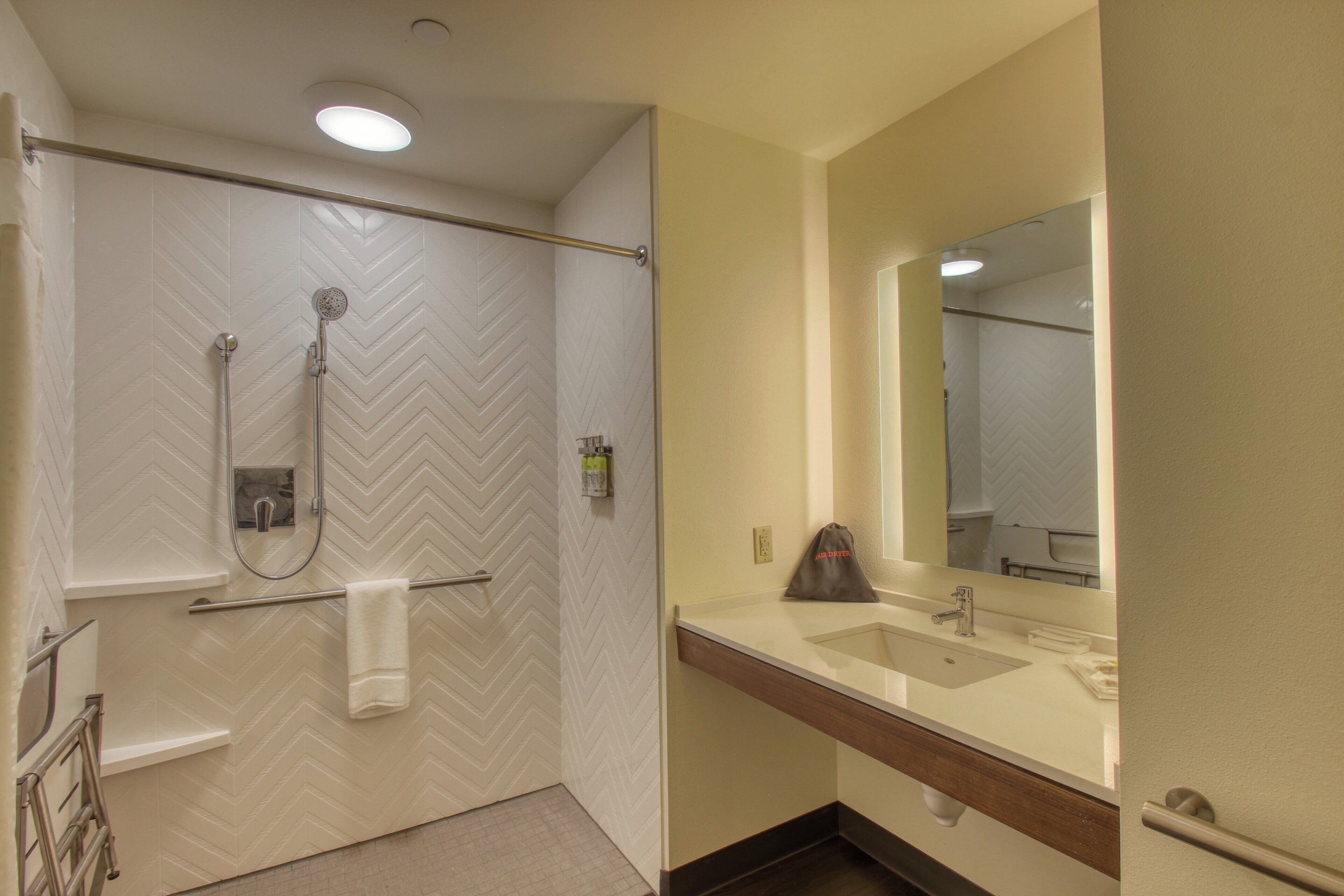 A bathroom with a shower, a sink, a mirror, and a towel rack.