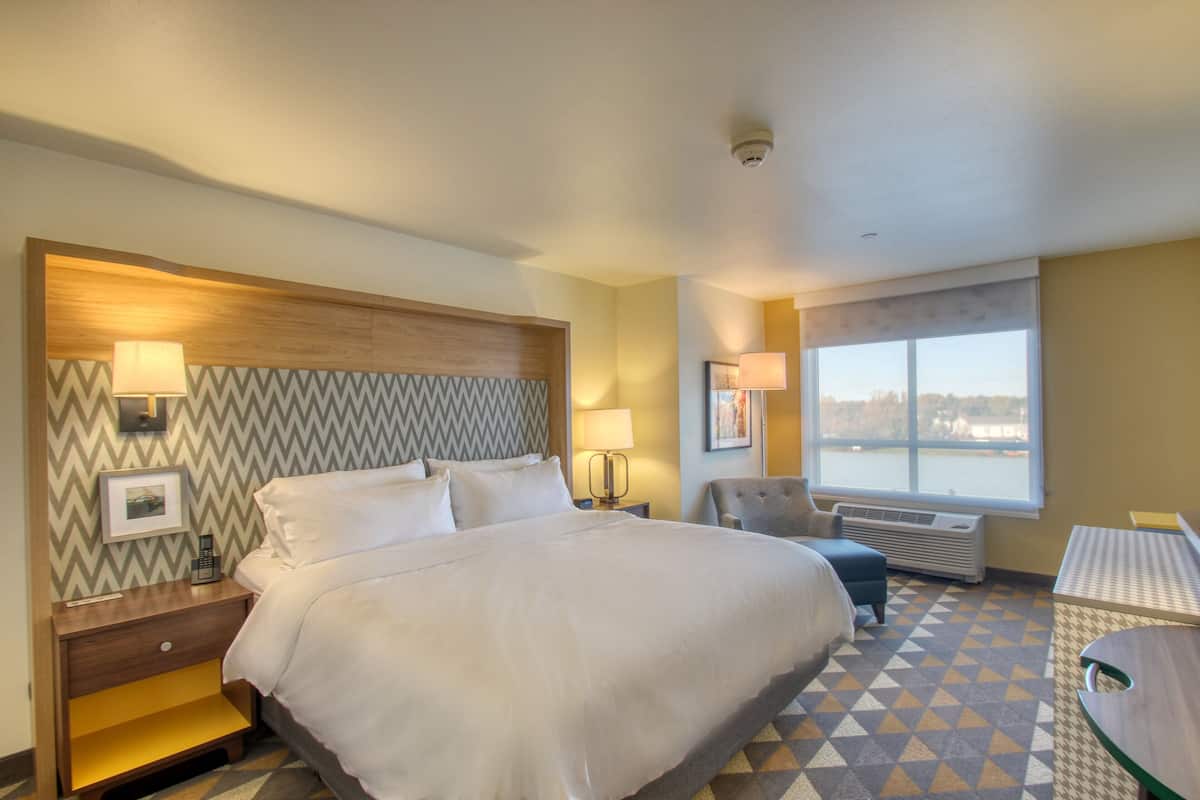 Habitación de hotel con una cama grande, un escritorio, una silla y vistas al exterior.
