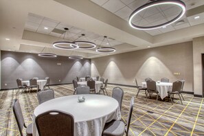Een vergaderzaal met ronde tafels, grijze stoelen en moderne ronde plafondlampen.