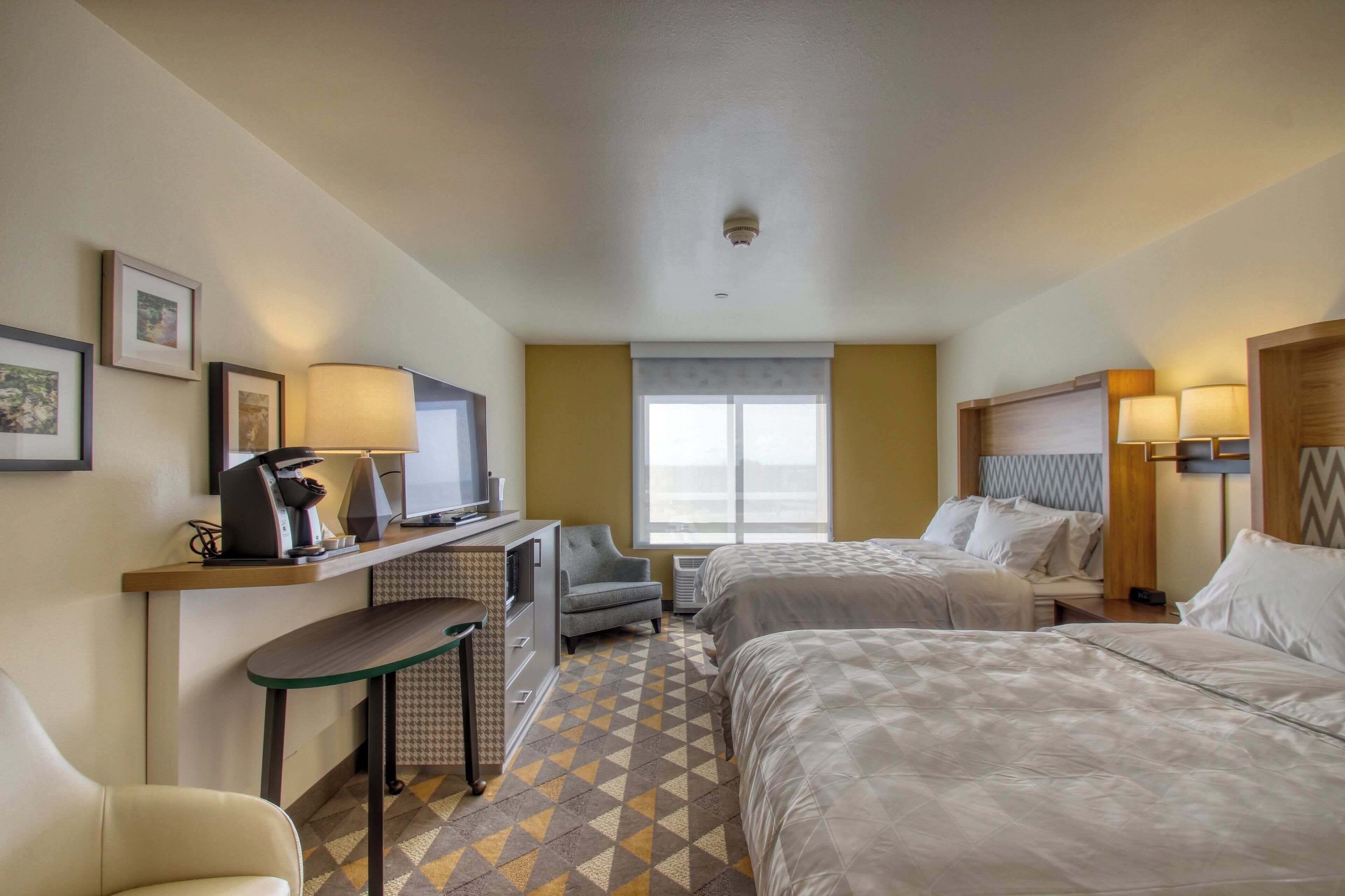 Habitación de hotel con dos camas, un escritorio con silla, televisor y ventana con vistas.